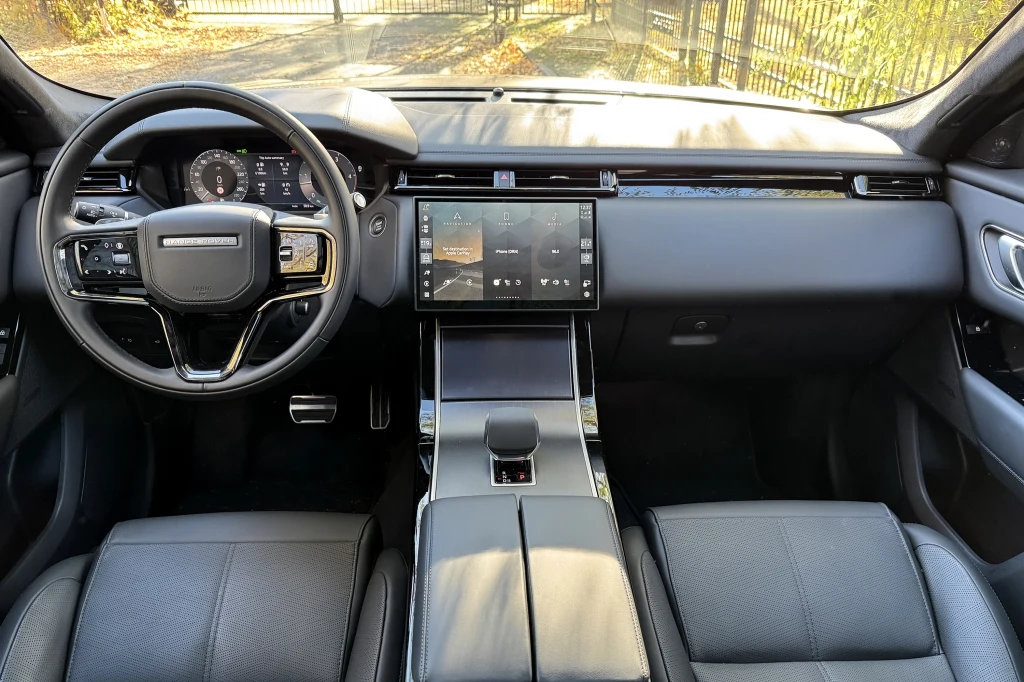 Nowoczesne wnętrze samochodu z dużym, dotykowym ekranem na konsoli centralnej, skórzanymi fotelami oraz panelem sterowania przy kierownicy, wszystko w eleganckim, minimalistycznym stylu.