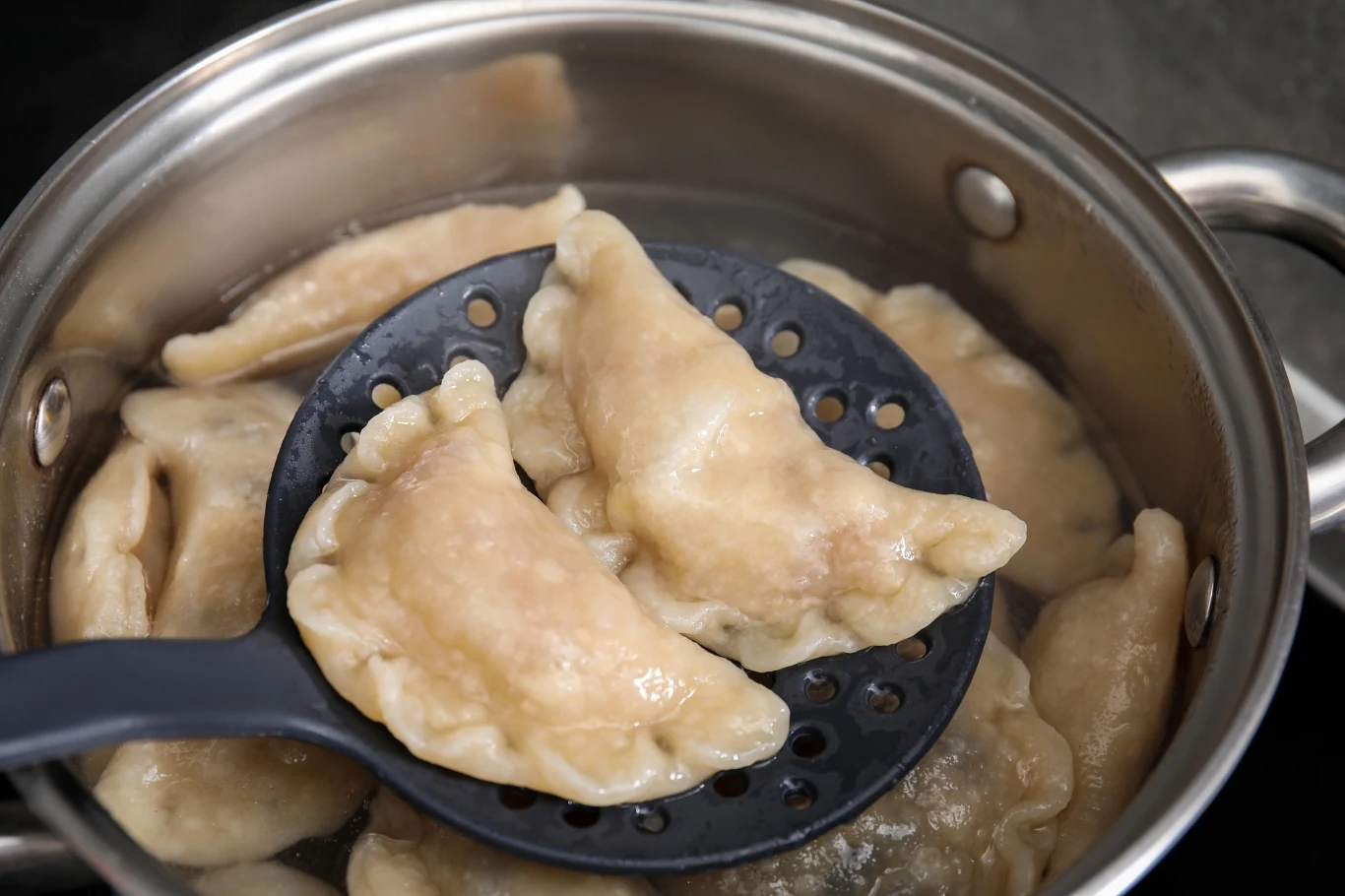 GIS ostrzega przed jednym z podbieraków do pierogów, który zawiera groźne substancje chemiczne / zdjęcie ilustracyjne Gotujące się pierogi wypływające na powierzchnię wody w garnku, część z nich uniesiona łyżką cedzakową.