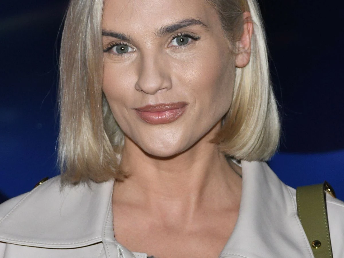 Karolina Gilon Kobieta o blond włosach, ubrana w jasną kurtkę, patrzy spokojnie w obiektyw na ciemnoniebieskim tle.