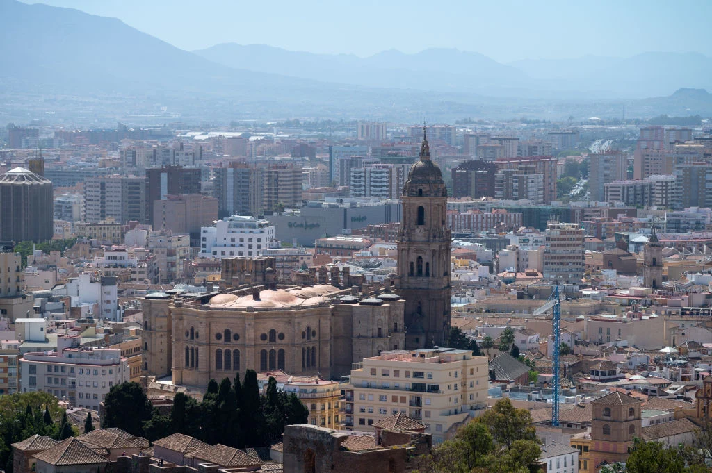 Katedra z charakterystyczną wieżą góruje nad rozległą zabudową miasta otoczoną gęstą tkanką miejską, w tle panorama gór i nowoczesne budynki mieszkalne.