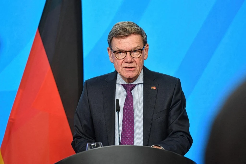 Skandaliczna aukcja pamiątek. MSZ Niemiec zabrało głos Starszy mężczyzna w okularach przemawia przy mównicy, w tle widoczna niemiecka flaga oraz niebieskie tło.