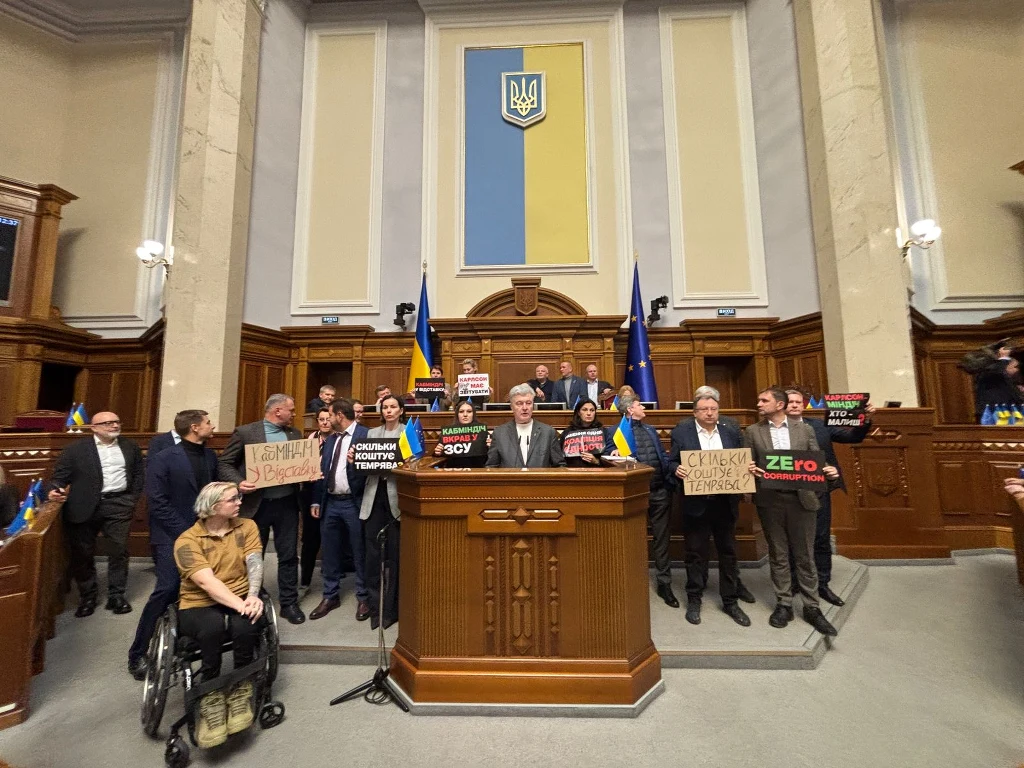 Awantura w ukraińskim parlamencie. Opozycja zablokowała posiedzenie Grupa polityków oraz działaczy z transparentami stojących za mównicą w sali obrad parlamentu. W tle widoczne flagi Ukrainy i Unii Europejskiej, a także godło Ukrainy na ścianie.