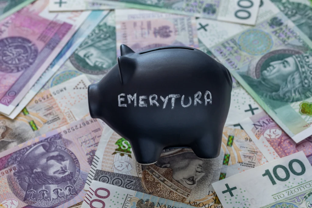 Jaka emerytura przy zarobkach 7000 zł brutto? Szacunki pokazują różne wartości, a oszczędzać na emeryturę warto jak najwcześniej także samemu. Czarna skarbonka z napisem 'Emerytura' stojąca na rozrzuconych banknotach polskich złotych różnych nominałów, symbolizująca oszczędzanie pieniędzy na przyszłość.