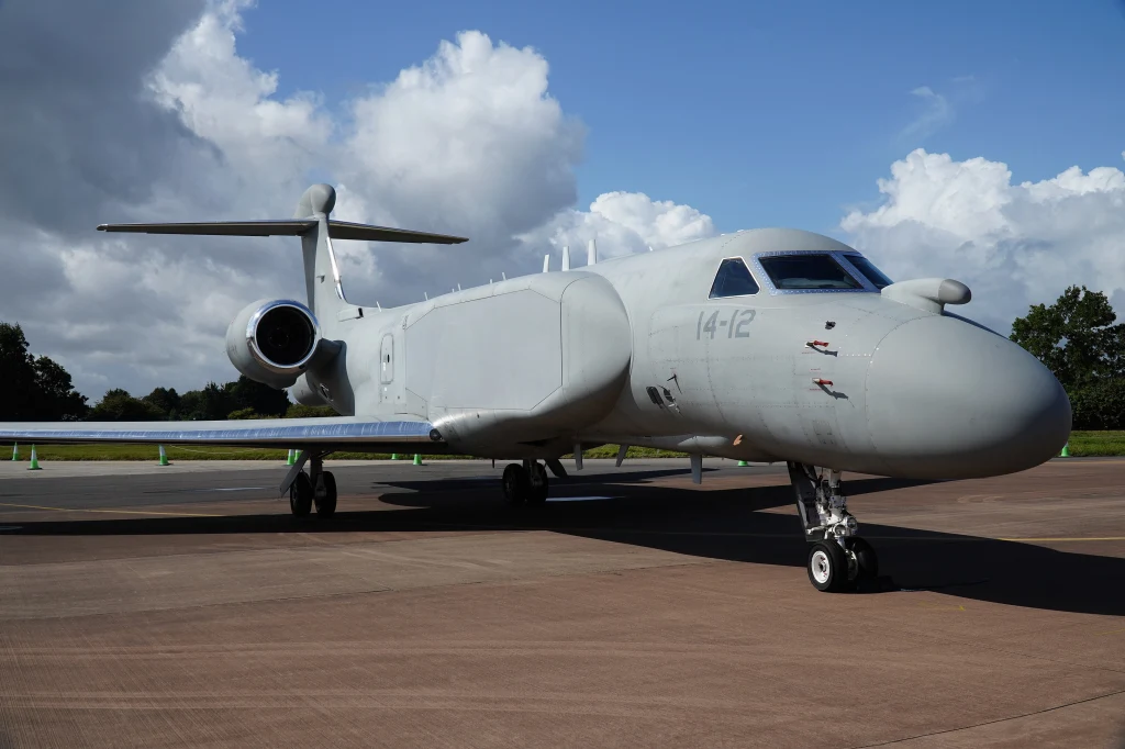 Włoski G550 CAEW był jednym z samolotów, który brał udział w obserwacji nieba podczas naruszenia polskiej przestrzeni powietrznej przez drony w nocy 9/10 września Wojskowy samolot rozpoznawczy o szarej barwie stoi zaparkowany na płycie lotniska, w tle widoczne chmury i fragment zieleni.