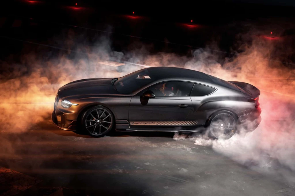 Czarny sportowy samochód w ruchu pokryty oparami dymu z kół, dynamiczne światło podkreśla sylwetkę pojazdu na tle ciemnego otoczenia.