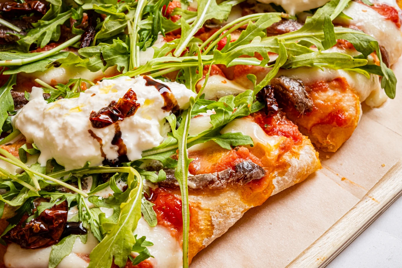 Rukola i pizza to połączenie znane i warto je wprowadzić Kawałki pizzy z cienkim ciastem, na których znajdują się pomidory, rukola, kremowy ser, suszone pomidory i sos balsamiczny.