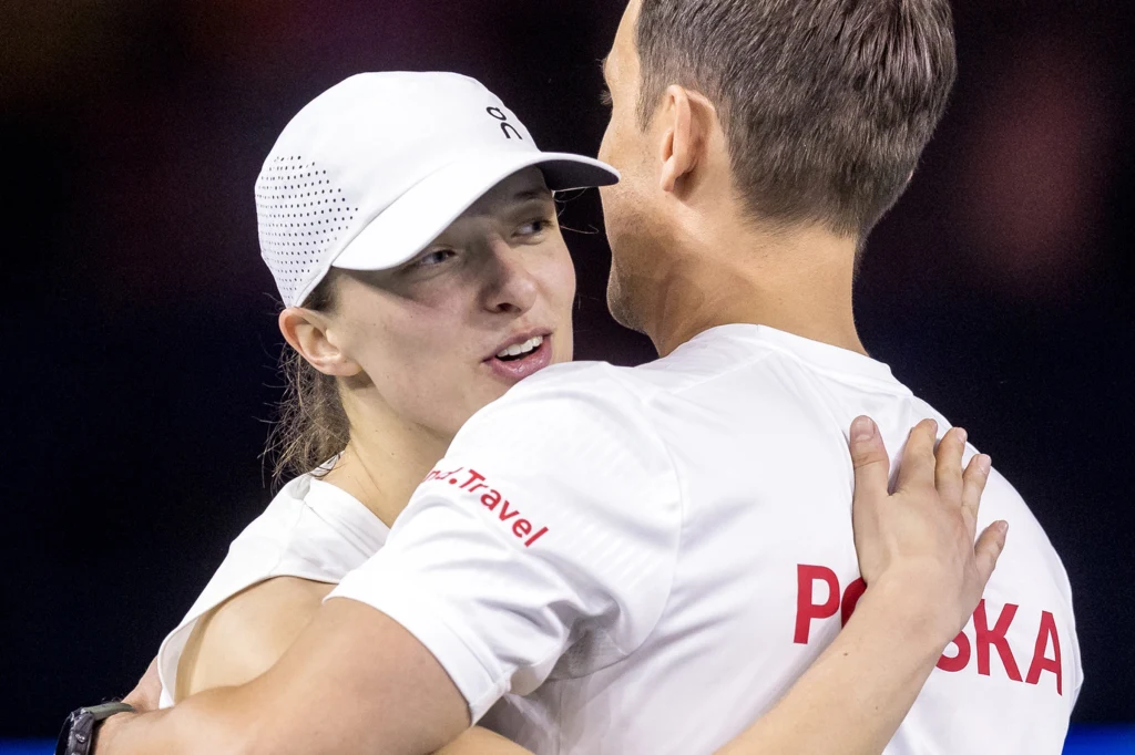 Czy Iga Świątek znów pomoże reprezentacji Polski w kwietniu? Już wiadomo, że będzie trochę łatwiej Dwie osoby w białych koszulkach obejmują się, jedna z nich ma na głowie białą czapkę z daszkiem, na plecach drugiej widoczne napisy Polska i Travel.