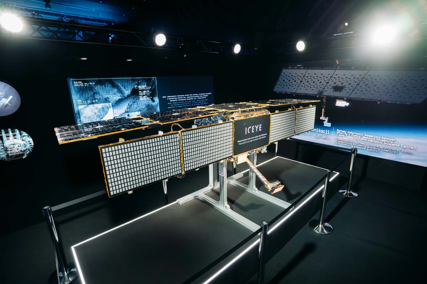 ICEYE zaprezentował model radarowego satelity, który zostanie wysłany na orbitę Model satelity ICEYE ustawiony w dobrze oświetlonej przestrzeni wystawienniczej z panelami słonecznymi i wyświetlonymi wizualizacjami na monitorach w tle.