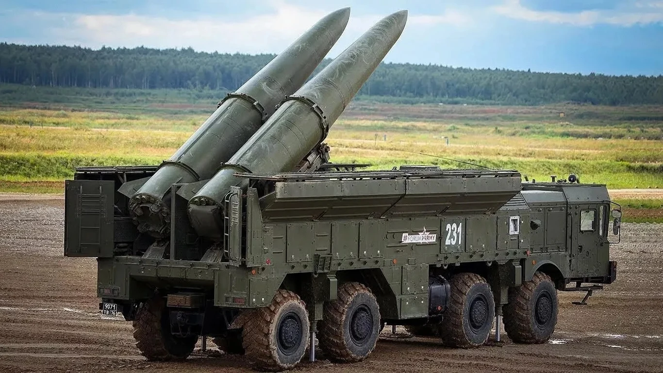 Rosjanie na masową skalę bombardują swój kraj Rosyjski system rakietowy krótkiego zasięgu Iskander osadzony na wieloosiowej platformie kołowej, z dwiema dużymi rakietami gotowymi do odpalenia, ustawiony na otwartym terenie z lasem w tle.