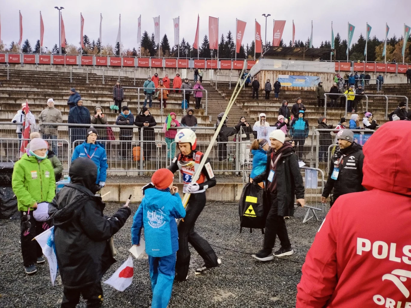 W czasie konkursu LGP w Klingenthal Kamil Stoch został zabrany do kontroli. Przyszedł po niego sam Mathias Hafele Zawodnik w stroju skoczka narciarskiego z nartami na ramieniu otoczony przez kibiców, w tle trybuny z widzami oraz osoby obsługi wydarzenia sportowego.