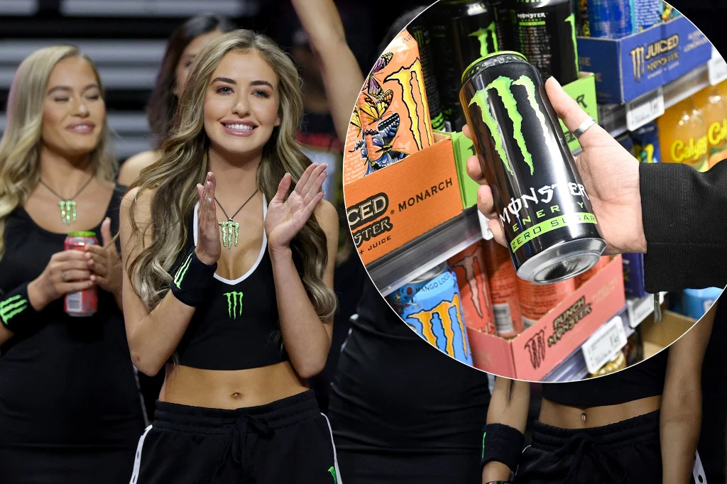 Uśmiechnięte kobiety ubrane w czarne stroje sportowe z logiem Monster Energy. Jedna z nich trzyma puszkę napoju Monster Energy, w tle produkty tej marki na sklepowej półce.