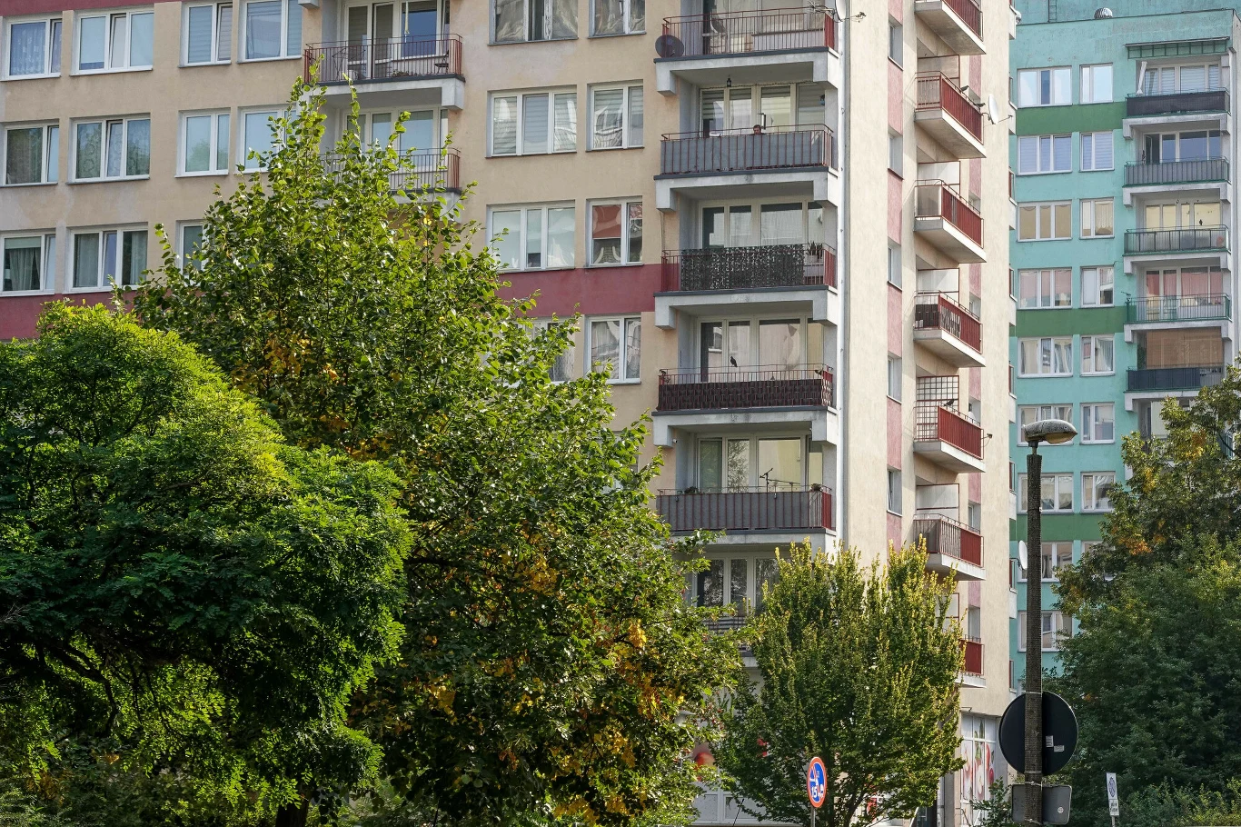 Spółdzielnie mieszkaniowe zyskają prawo do użytkowania wieczystego gruntów, których status jest nieuregulowany od czasów PRL Wysoki blok mieszkalny z licznymi balkonami i oknami, otoczony zielonymi drzewami, w tle kolejny budynek mieszkalny o podobnej architekturze.
