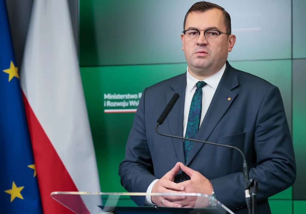 Minister rolnictwa Stefan Krajewski podsumował dotychczasowe działania dotyczące rozwiązywania afery związanej z działką CPK w Zabłotni Mężczyzna w garniturze stojący za mównicą, w tle polska i unijna flaga oraz zielona tablica z napisem Ministerstwo Rolnictwa i Rozwoju Wsi, oficjalna atmosfera i prezentacja.