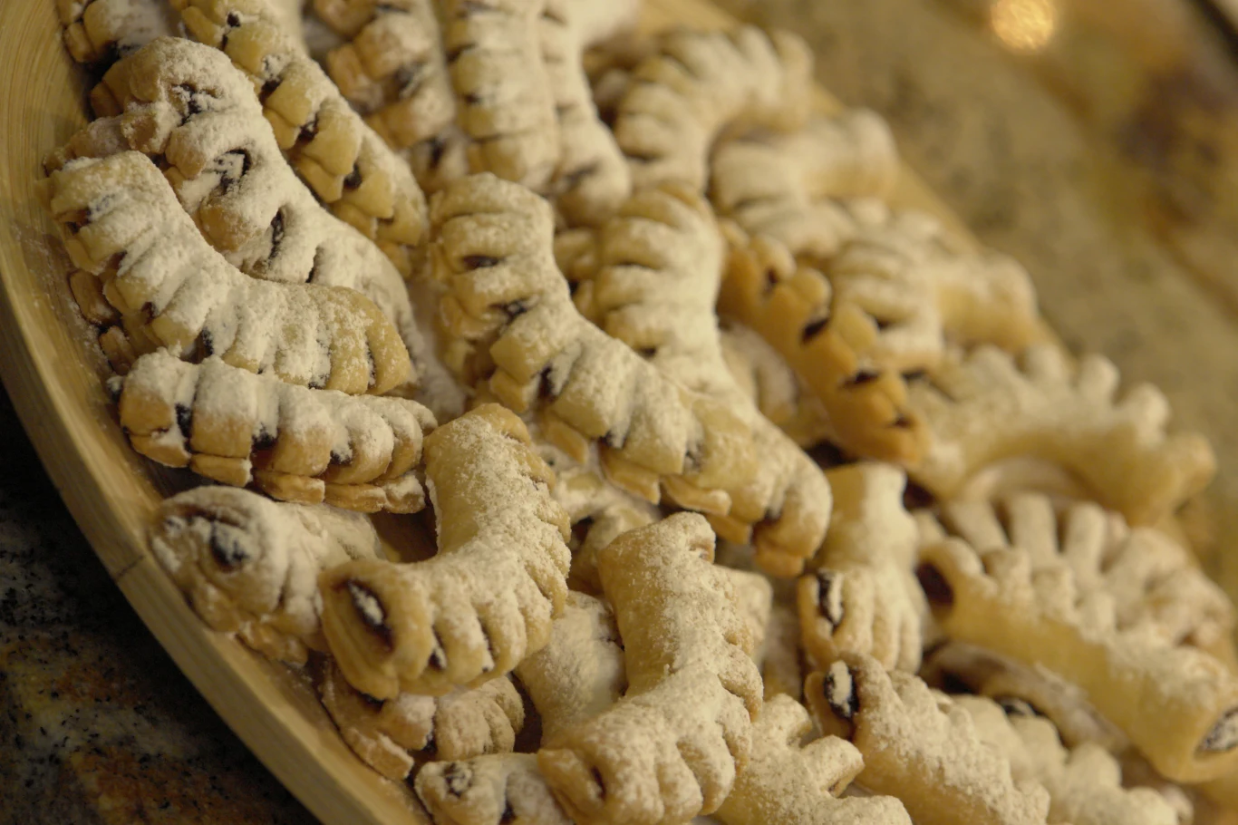 Ciastka grzebyczki Na drewnianej tacy ułożone ciasteczka w kształcie półksiężyców, posypane cukrem pudrem, z widocznym nadzieniem w środku.