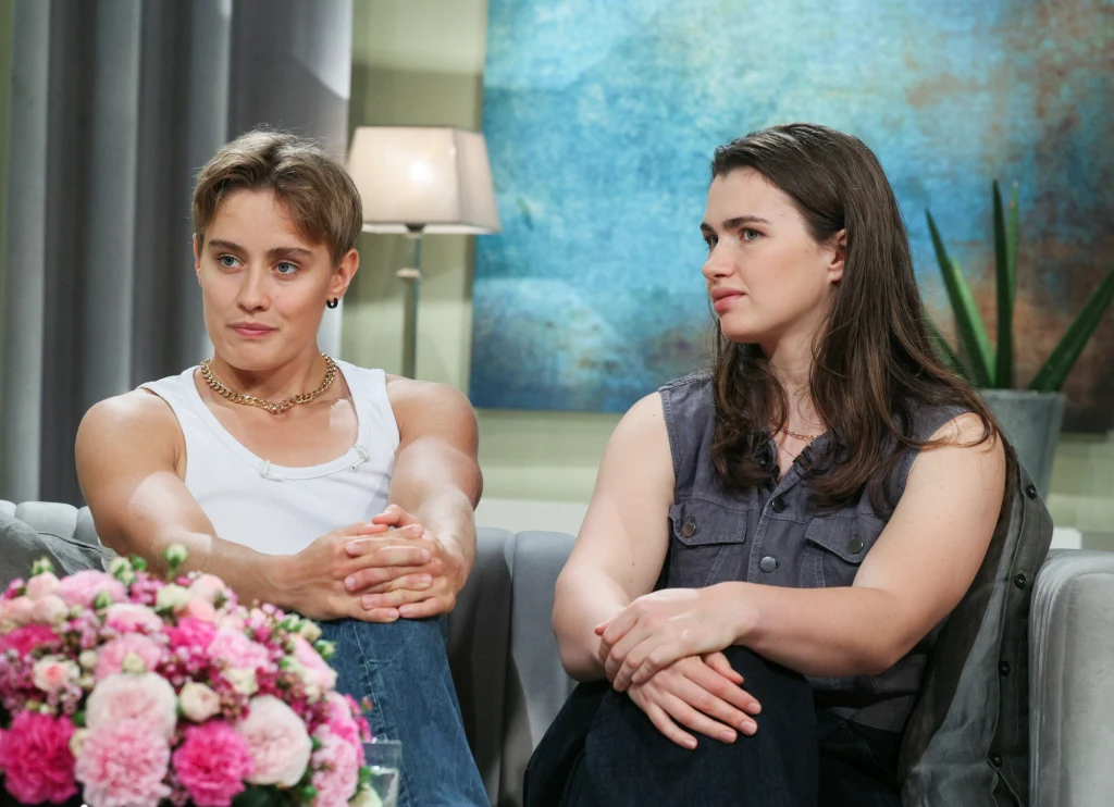 Katarzyna Zillmann i Julia Walczak w programie "Demakijaż" Dwie młode osoby siedzące na kanapie w jasnym, eleganckim wnętrzu, w tle lampa i obraz na ścianie, na pierwszym planie bukiet różowych kwiatów.