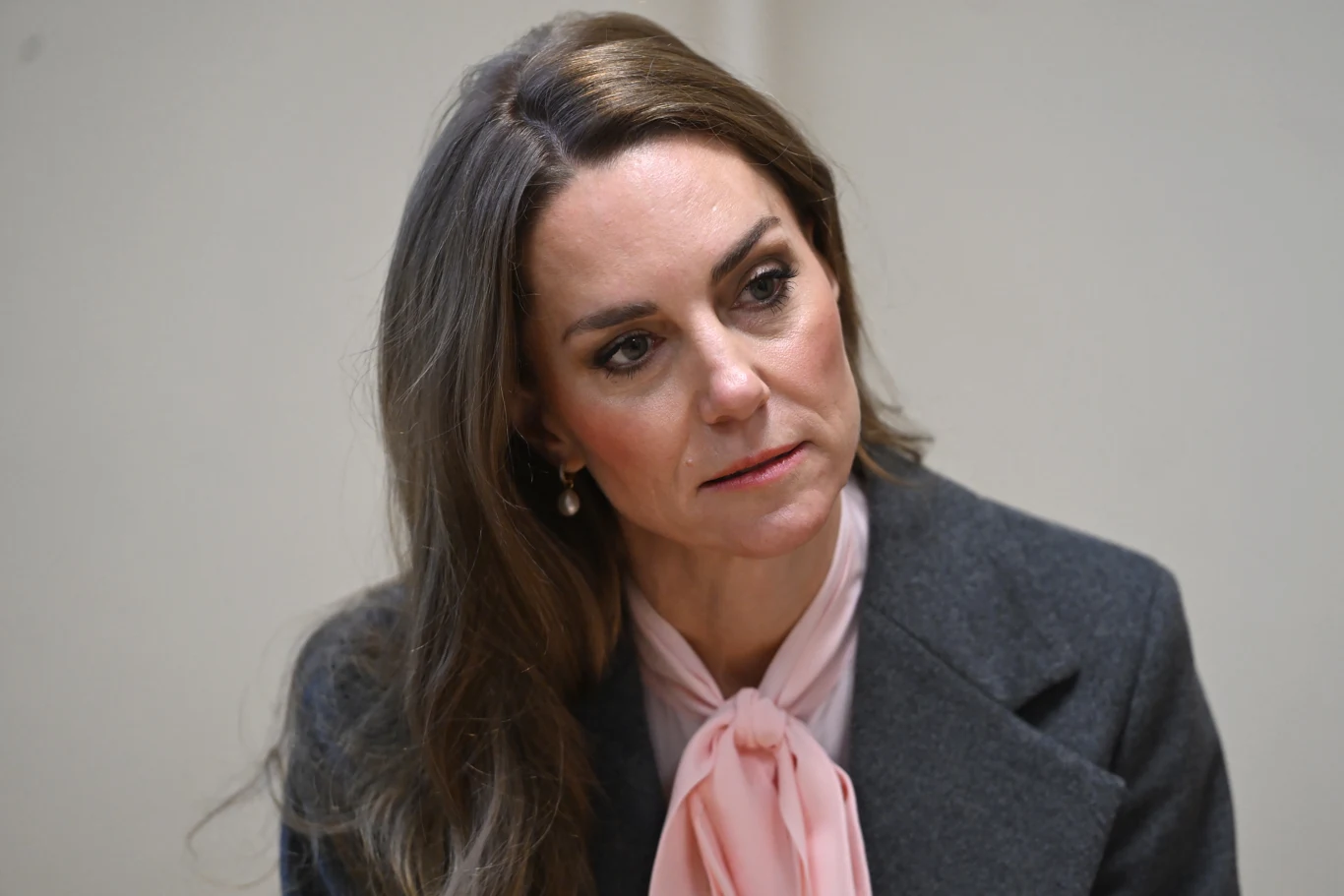 Kobieta o długich, brązowych włosach, ubrana w szary żakiet oraz jasnoróżową bluzkę z kokardą pod szyją, patrząca lekko w bok o poważnym wyrazie twarzy, na jasnym tle.