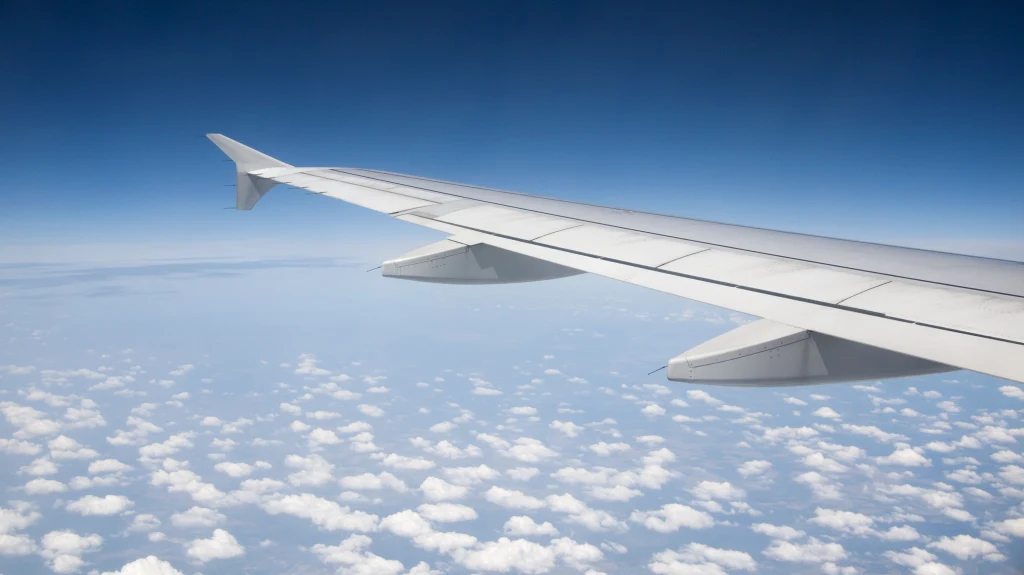 Widok na skrzydła i silniki jest kluczowy dla członków załogi Skrzydło samolotu na tle błękitnego nieba z widocznymi białymi chmurami pod nim.