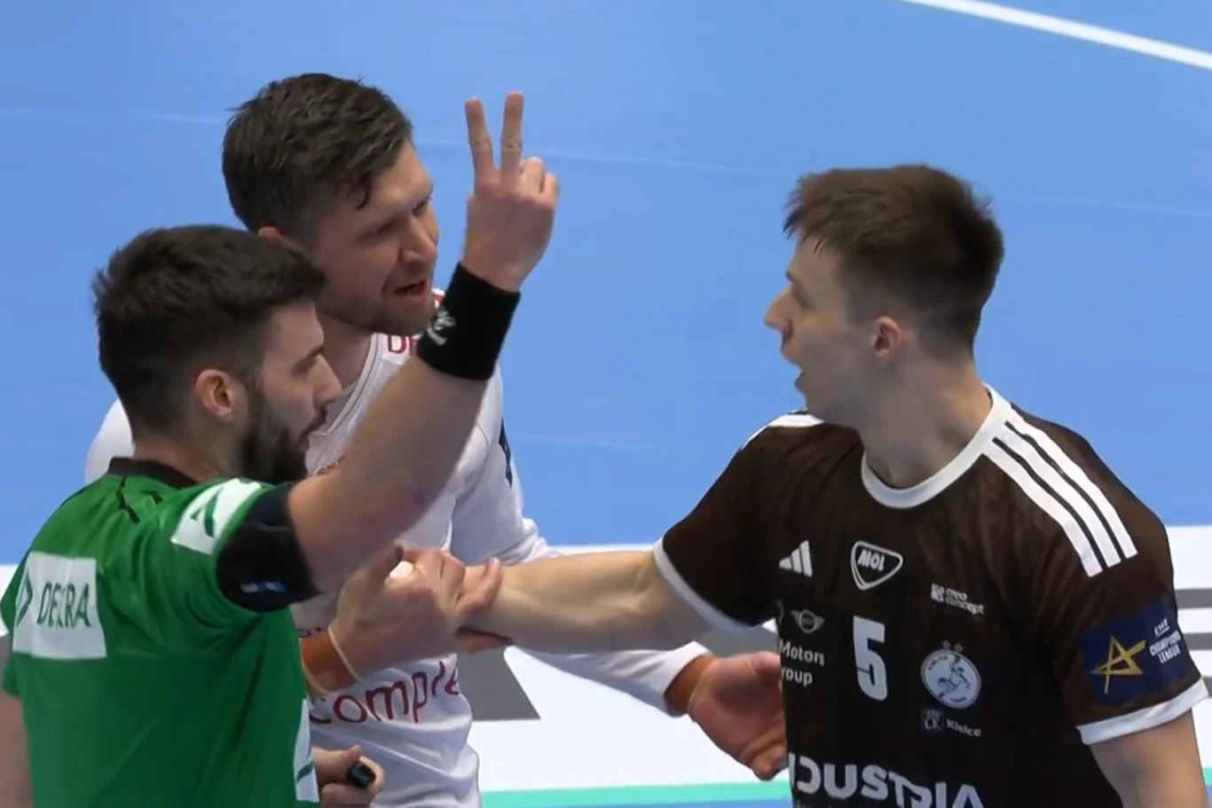 Niklas Landin miał pretensje do Michała Olejniczaka za rzut w okolice głowy. Zawodnik Industrii wyleciał z boiska Sędzia w zielonym stroju pokazuje dwóm zawodnikom sygnalizację palcami podczas intensywnej dyskusji na boisku do piłki ręcznej. Obaj zawodnicy stoją naprzeciw siebie ubrani w różne stroje meczowe, a w tle widoczny jest fragment niebieskiego parkietu.