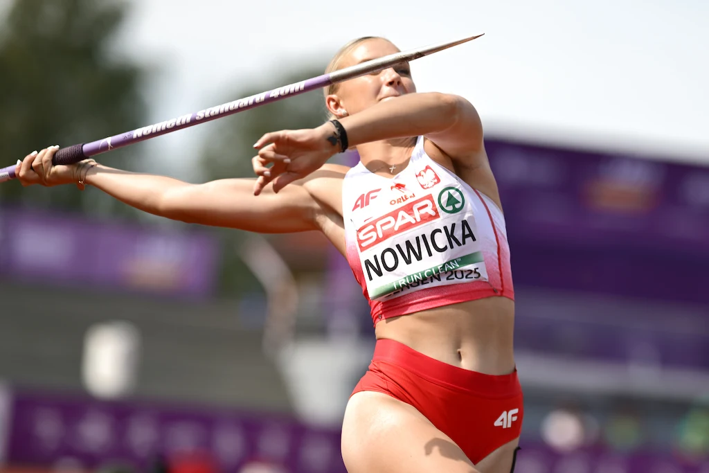 Zawodniczka w trakcie rzutu oszczepem podczas zawodów lekkoatletycznych, ujęcie dynamiczne z widocznym ruchem i skupieniem na twarzy, na stroju numery i nazwisko Nowicka.