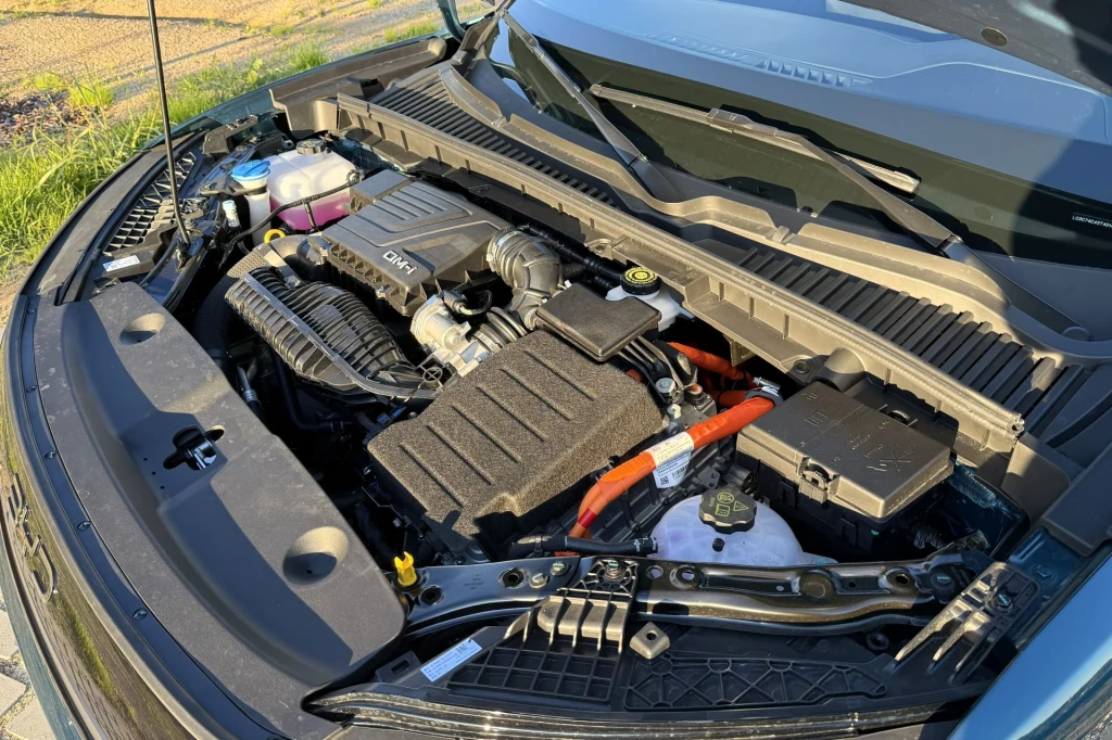 Otwarta maska samochodu odsłaniająca silnik z widocznymi elementami mechanicznymi oraz przewodami, w tym także przewodami elektrycznymi typowymi dla napędu hybrydowego. Silnik oraz komponenty znajdują się w czystej komorze, światło słoneczne podkreśla ...