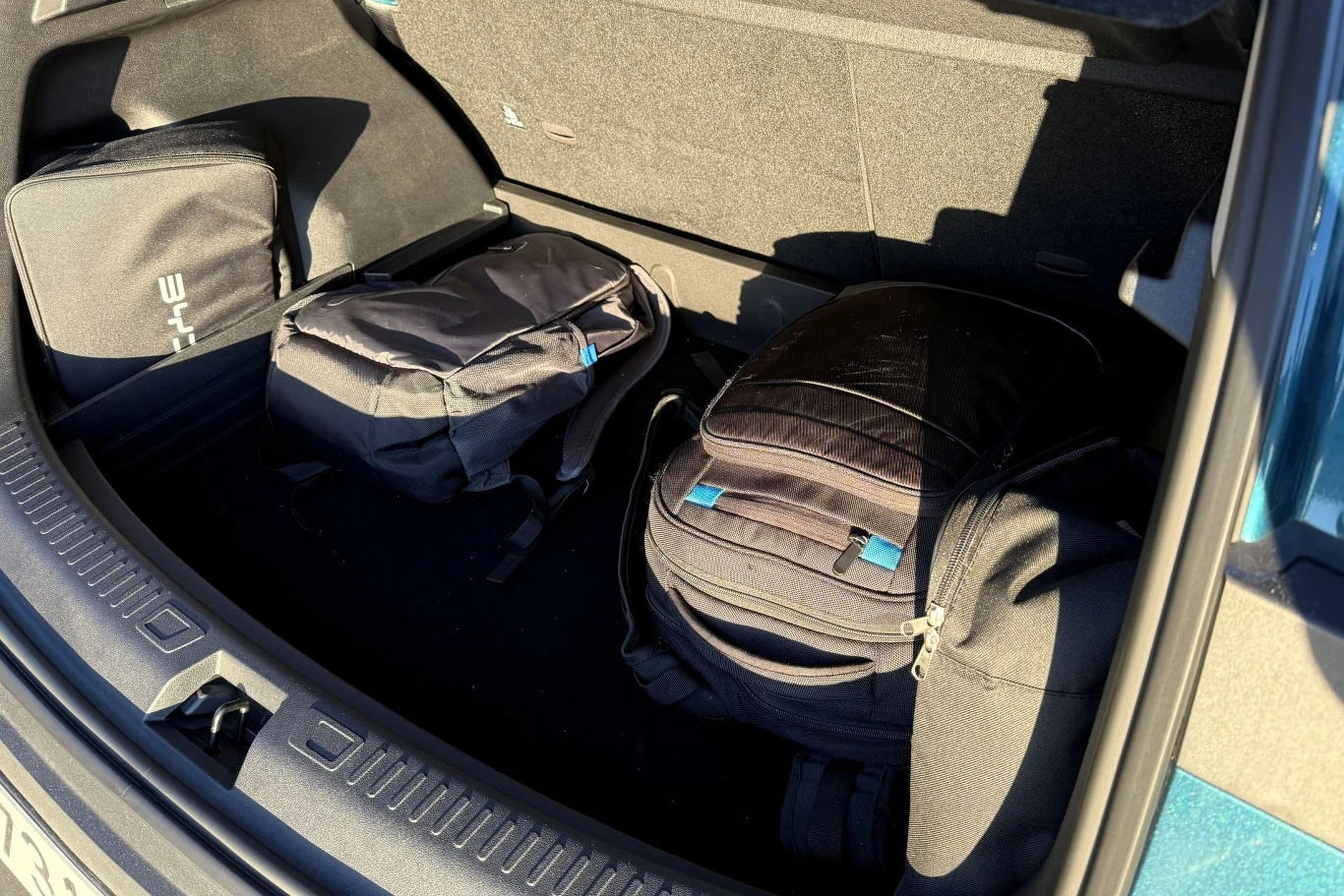 Bagażnik BYD Atto 2 DM-i mieści 425 litrów. Trzy czarne torby podróżne ułożone w bagażniku samochodu, z czego dwie mają jasno widoczne niebieskie akcenty na suwakach. Wnętrze bagażnika oświetlone jest naturalnym światłem.