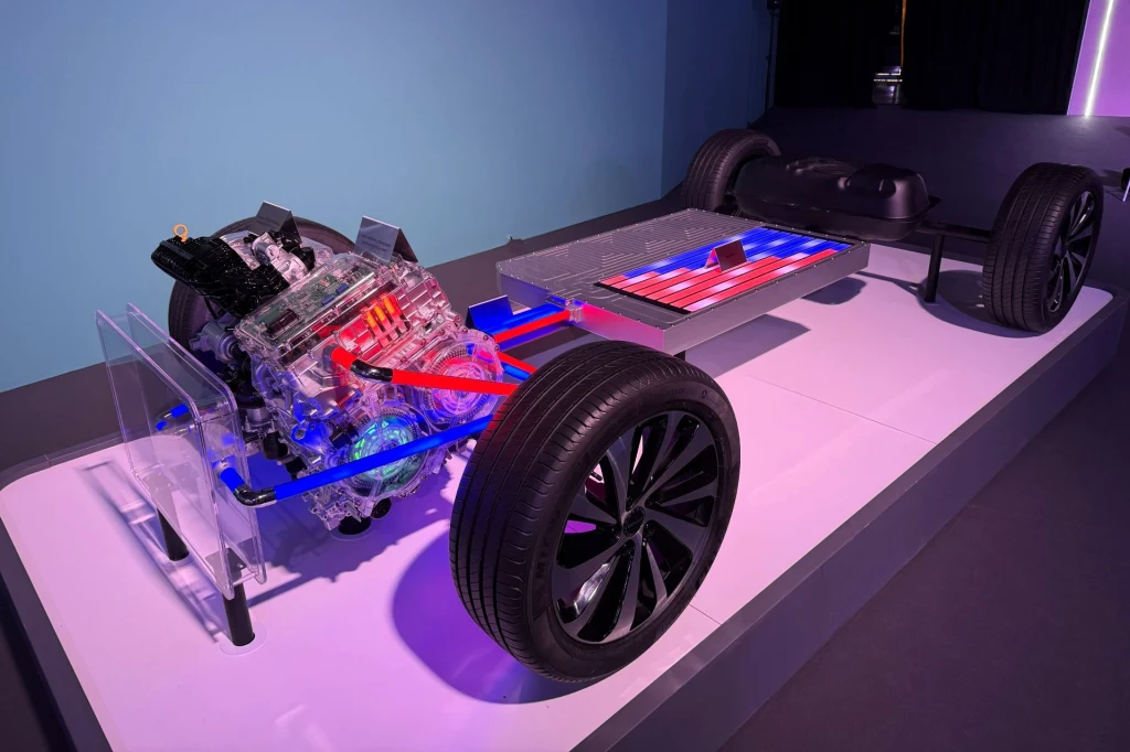 Model podwozia samochodu elektrycznego z wyraźnie widocznym silnikiem elektrycznym, układem przeniesienia napędu oraz dużą baterią trakcyjną, całość oświetlona kolorowymi światłami, z wyeksponowanymi kołami.