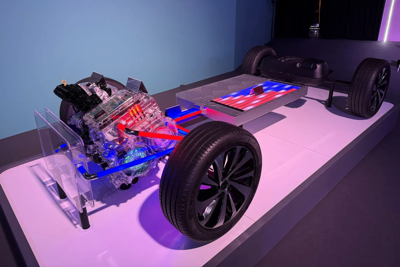 Z reguły silnik spalinowy ładuje akumulator, ale jeżeli układ będzie potrzebował dodatkowej mocy, benzynowa jednostka przekaże moc bezpośrednio do kół. Model podwozia samochodu elektrycznego z wyraźnie widocznym silnikiem elektrycznym, układem przeniesienia napędu oraz dużą baterią trakcyjną, całość oświetlona kolorowymi światłami, z wyeksponowanymi kołami.