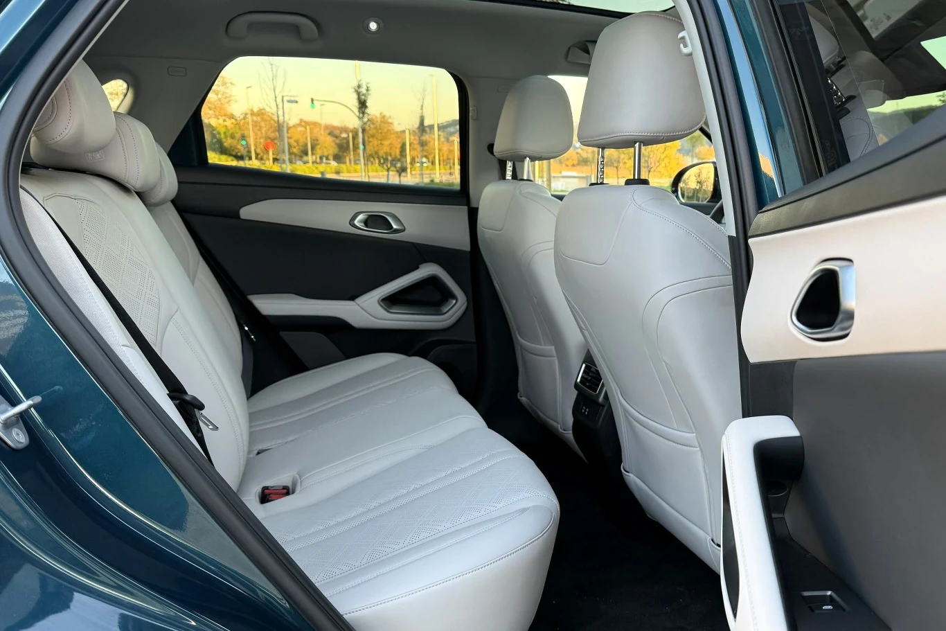 Rozstaw osi na poziomie 2,62 m oraz płaska podłoga z tyłu sprawiają, że BYD Atto 2 w obu wariantach napędu można podróżować bardzo wygodnie. Wnętrze tylnej części samochodu z jasnymi, skórzanymi siedzeniami, otwartymi drzwiami i widokiem przez okno na kolorowe drzewa. Przestronne, czyste i nowoczesne wyposażenie auta.