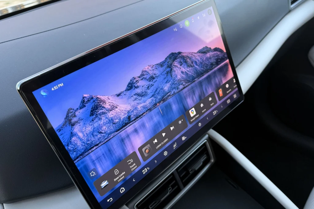 Komputerowy wyświetlacz dotykowy zamontowany w desce rozdzielczej samochodu, na ekranie wyświetlony krajobraz gór ze śniegiem oraz różne ikony aplikacji i ustawień multimedialnych.
