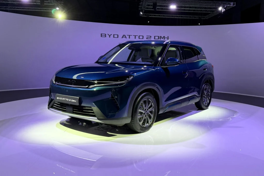 Nowoczesny SUV BYD Atto 2 DM-i ustawiony na jasnej, podświetlonej platformie wystawowej z wyrazistymi liniami nadwozia i ciemnoniebieskim lakierem, otoczony minimalistycznym tłem z nazwą modelu umieszczoną na panelu za pojazdem.