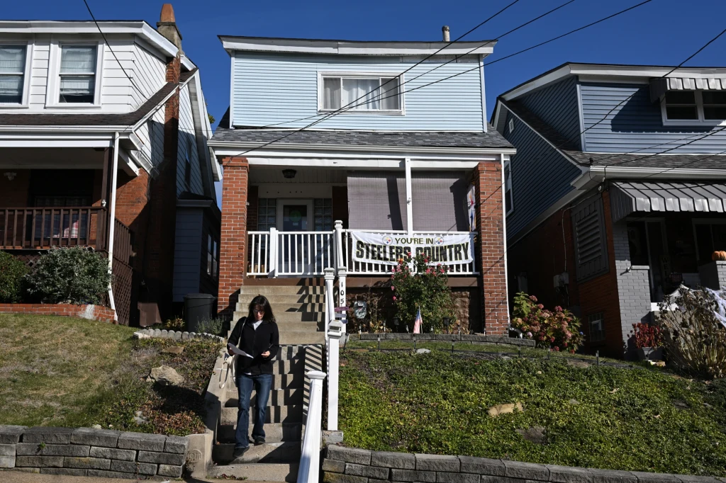 Dom jednorodzinny z cegły i sidingu z banerem w stylu sportowym na werandzie, schody prowadzące do wejścia, kobieta schodząca po schodach, sąsiednie domy po obu stronach, spokojna okolica.