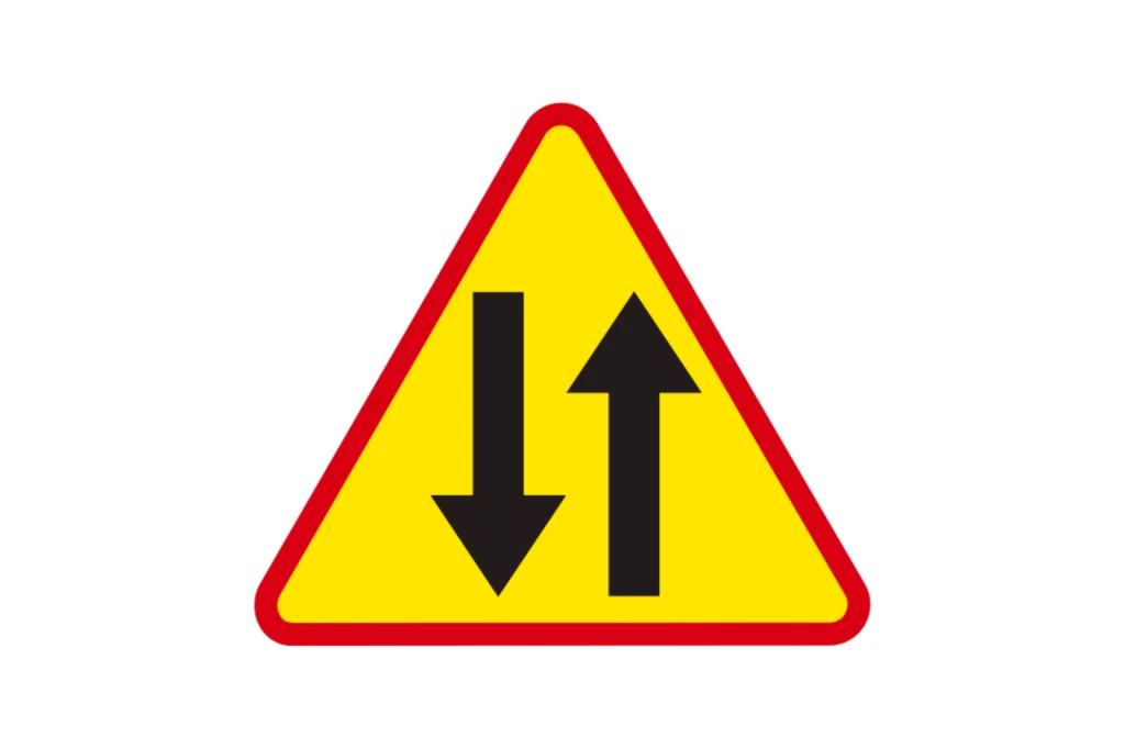 Trójkątny znak drogowy z czerwoną obwódką na żółtym tle, przedstawiający dwie czarne strzałki skierowane w przeciwnych kierunkach, symbolizujące ruch dwukierunkowy.