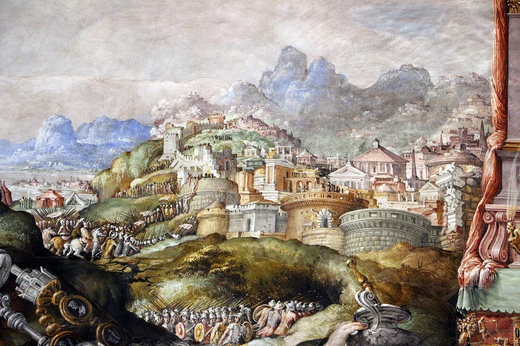 Panorama starożytnego miasta otoczonego murami, z licznymi budowlami i wieżami. Wokół fortyfikacji zgromadzone są liczne grupy żołnierzy i wojska, widoczne są elementy uzbrojenia i sztandary. W tle widoczne malownicze wzgórza oraz pozostałości większyc...