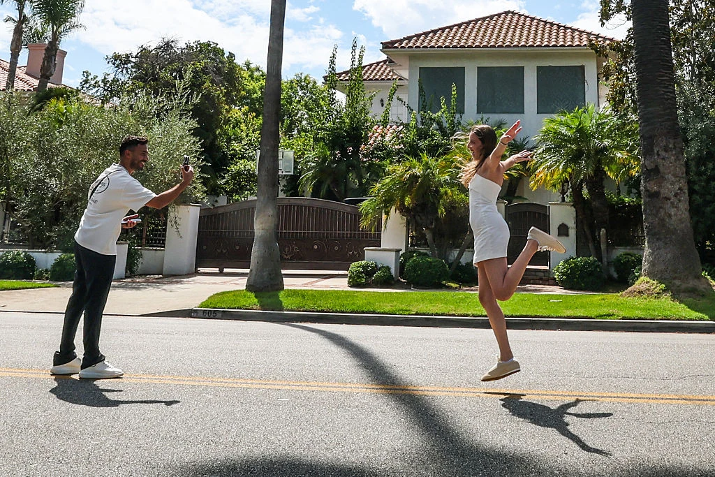 Media społecznościowe przestają być cool? Mężczyzna robi zdjęcie kobiecie skaczącej na pustej ulicy. Oboje uśmiechnięci, kobieta ubrana w białą sukienkę, w tle widoczny dom z palmami i zielonymi krzewami otoczony ogrodzeniem.