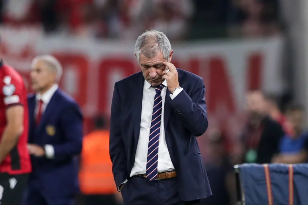 Po porażce z Albanią Fernando Santos przestał być selekcjonerem reprezentacji Polski Starszy mężczyzna w garniturze i krawacie, z poszarzałymi włosami, stoi ze spuszczoną głową i dotyka dłonią twarzy w geście zadumy lub rozczarowania. W tle inne osoby oraz nieostre fragmenty transparentu lub baneru.