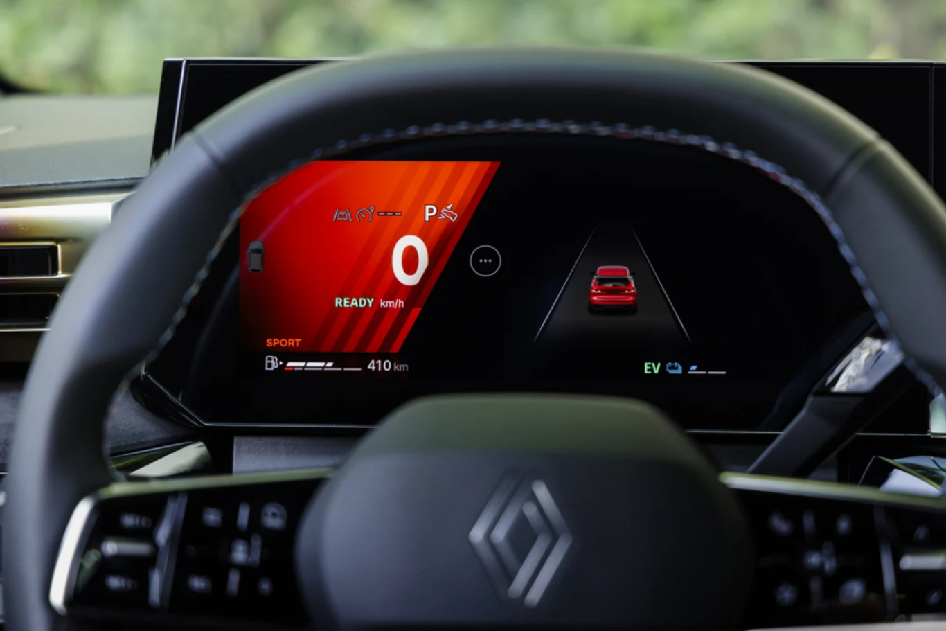 Kokpit nowoczesnego samochodu z cyfrowym wyświetlaczem, na którym widoczna jest prędkość, symbol auta oraz informacje dotyczące trybu jazdy i zasięgu pojazdu. Kierownica z logo producenta znajduje się na pierwszym planie.