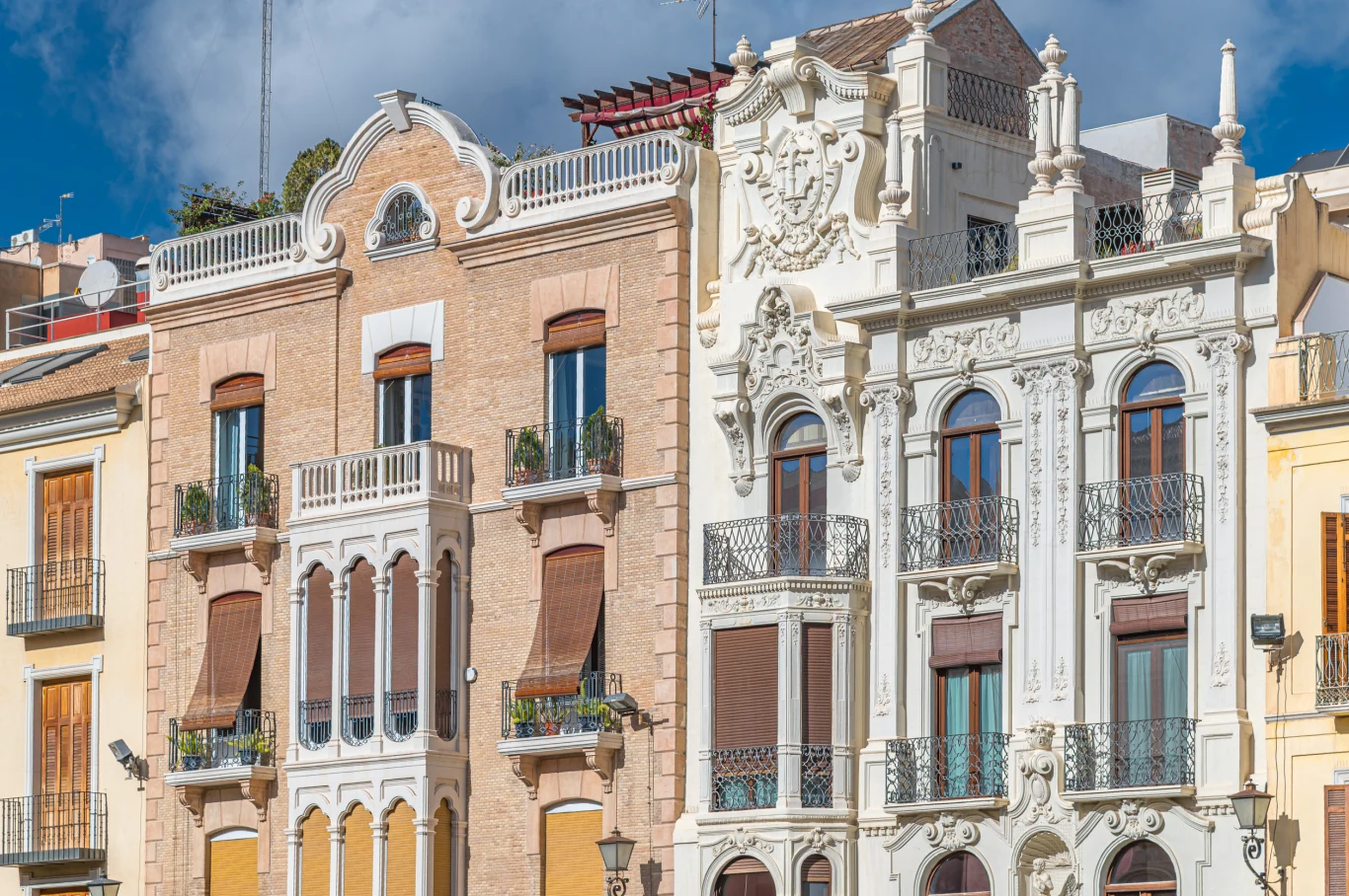 Fasady zabytkowych kamienic z charakterystycznymi zdobieniami i balkonami w stylu secesyjnym, jasne elewacje z licznymi oknami oraz szczegółowymi ornamentami.