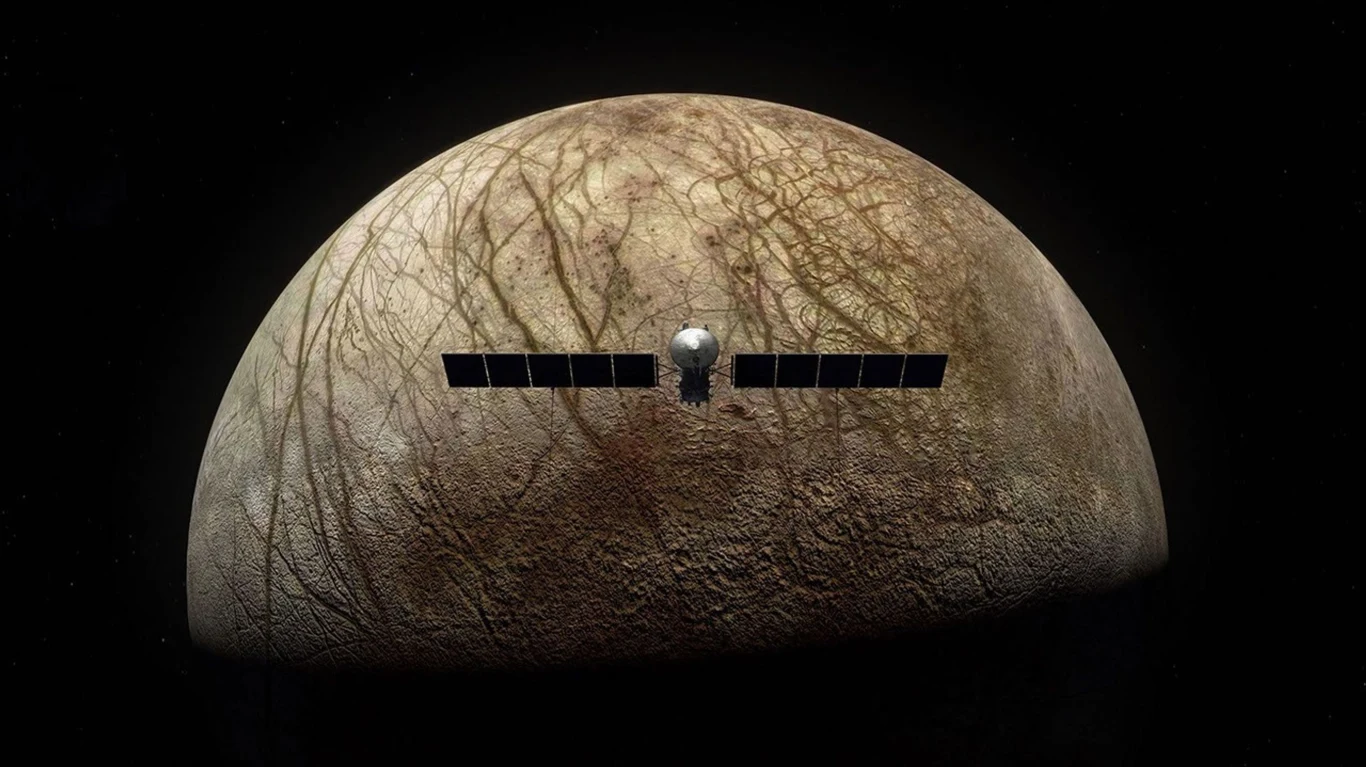 Sonda kosmiczna unosząca się nad powierzchnią Europy, jednego z księżyców Jowisza, widoczne charakterystyczne lodowe pęknięcia i brunatne linie na powierzchni ciała niebieskiego, ciemne tło kosmosu.