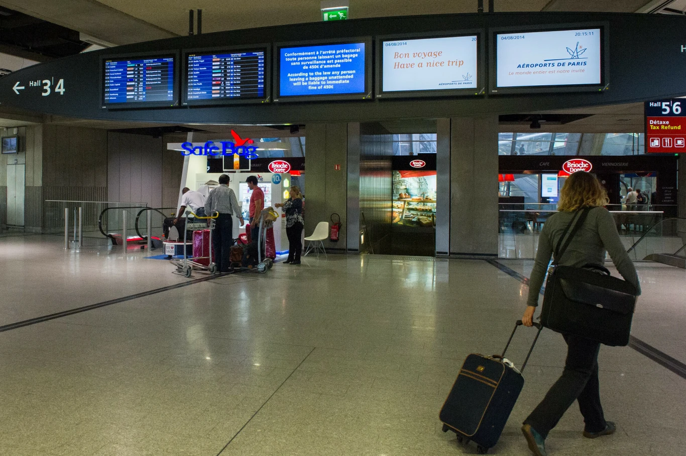 Francja będzie karać pasażerów za "antyspołeczne" zachowania w samolotach Hala lotniska z tablicami odlotów i przylotów oraz grupą ludzi przy windzie z wózkami bagażowymi, osoba z walizką na kółkach idąca w stronę przejścia.