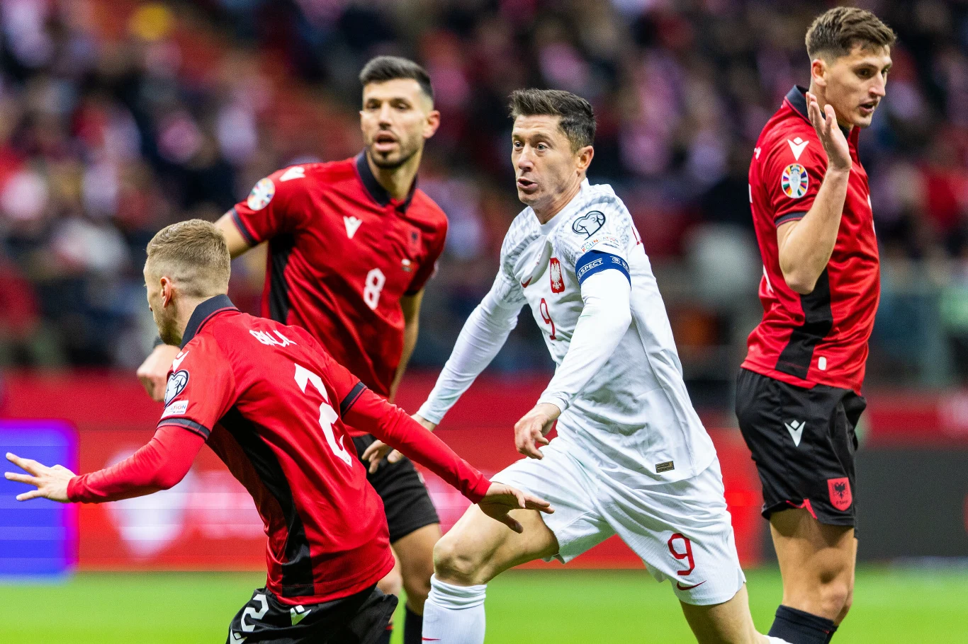 Robert Lewandowski w meczu Polska - Albania, 27.03.2023 r. Czterech piłkarzy w trakcie meczu, dwóch w czerwonych strojach reprezentacji Albanii i dwóch w białych strojach reprezentacji Polski, intensywnie walczących o piłkę na boisku.