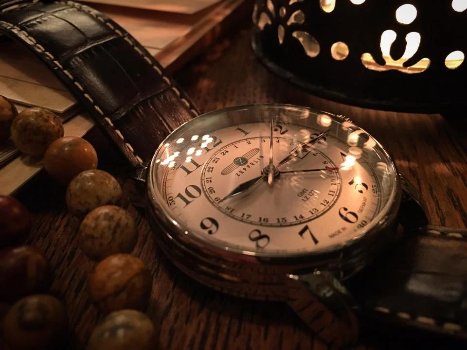 Vintage – ponadczasowy styl Stylowy zegarek na skórzanym pasku leżący na drewnianym stole w otoczeniu paciorków i notatek. Delikatne światło tworzy nastrojowy klimat, podkreślając detale tarczy oraz fakturę materiałów.