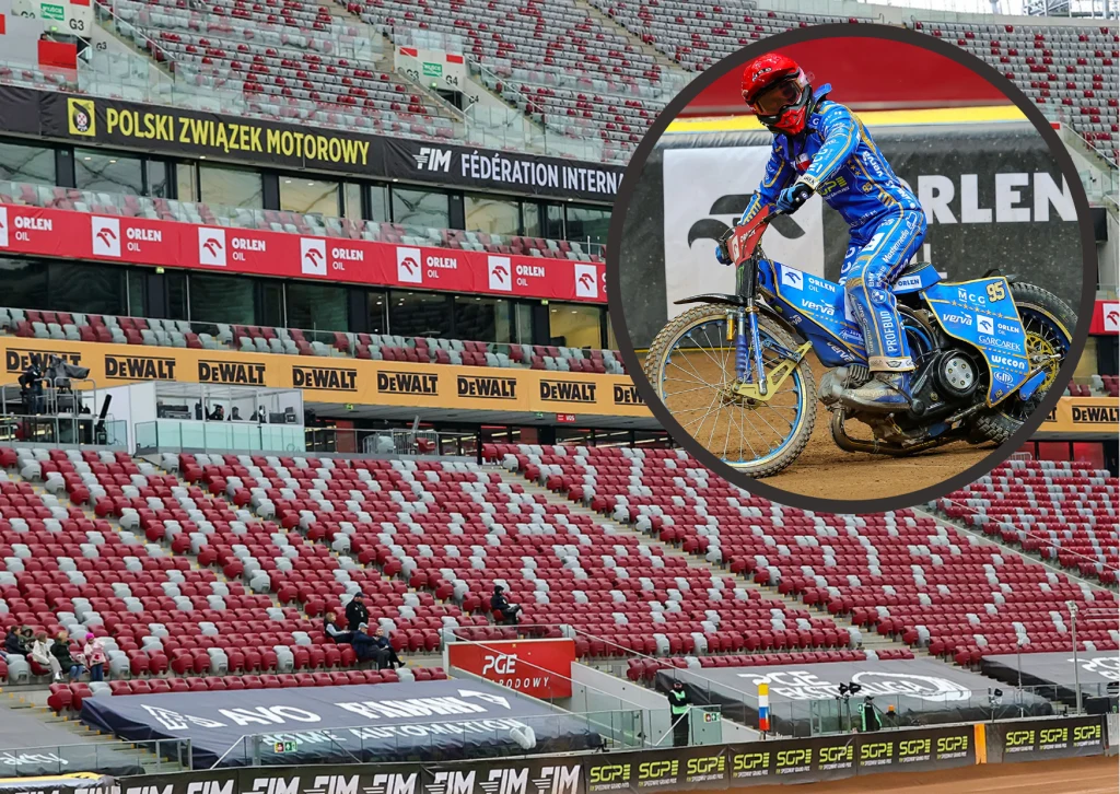 Motocyklista ubrany w strój ochronny niebieskiego koloru na motocyklu żużlowym podczas wyścigu na stadionie, widoczne puste trybuny oznaczone czerwonymi i białymi krzesełkami, banery sponsorsko-reklamowe i napisy organizatorów.