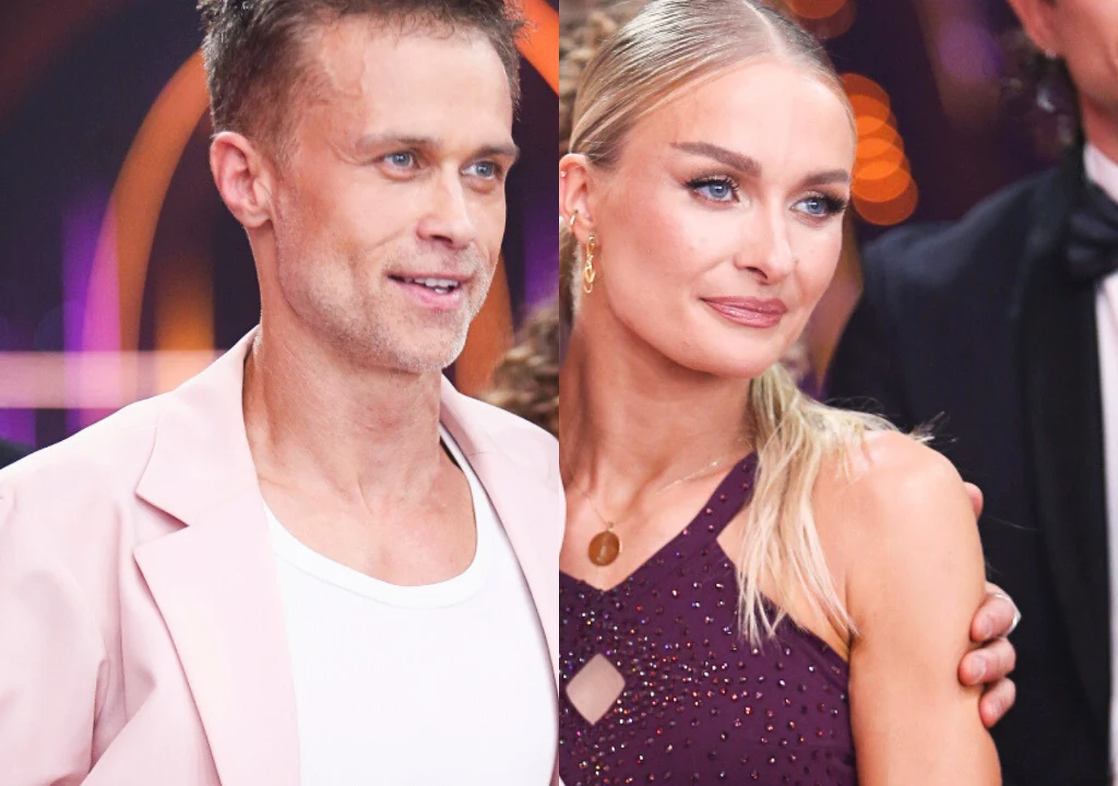 Dwójka elegancko ubranych osób, kobieta w ciemnofioletowej kreacji z długimi blond włosami spiętymi w kucyk i mężczyzna w jasnej marynarce oraz białej koszulce, stoją blisko siebie na tle kolorowych świateł.