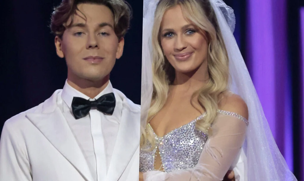 Mężczyzna w białym smokingu z czarną muszką oraz kobieta w białej sukni ślubnej i welonie uśmiechają się stojąc obok siebie na tle fioletowych świateł.