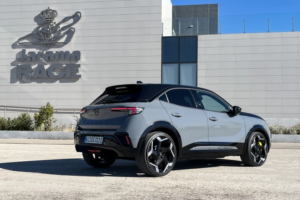 Nowoczesny szary samochód zaparkowany na placu przed budynkiem z napisem Jarama RACE oraz dekoracyjnym logo na ścianie, wyraźne sportowe felgi i minimalistyczna architektura w tle.