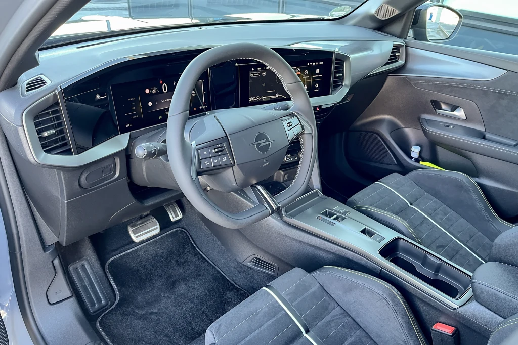Nowoczesna deska rozdzielcza z cyfrowym wyświetlaczem, wielofunkcyjna kierownica z logo marki Opel, sportowe fotele obite materiałem i skórą, elegancka konsola środkowa oraz aluminiowe pedały, całość utrzymana w ciemnej kolorystyce.