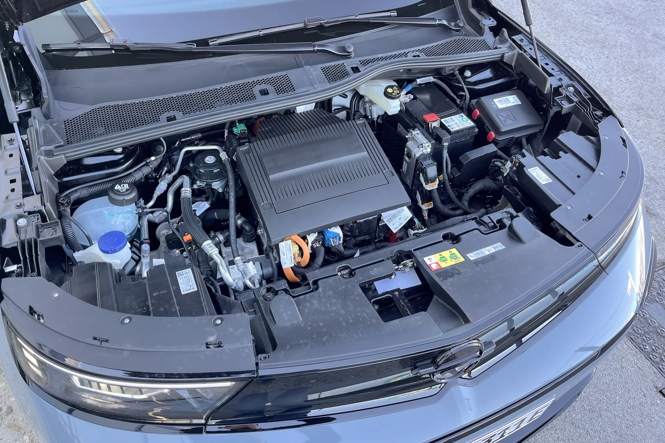 Otwarta maska samochodu ukazująca silnik elektryczny oraz pozostałe elementy komory silnika, wyraźnie widoczne akumulatory, przewody i zbiorniki płynów eksploatacyjnych.