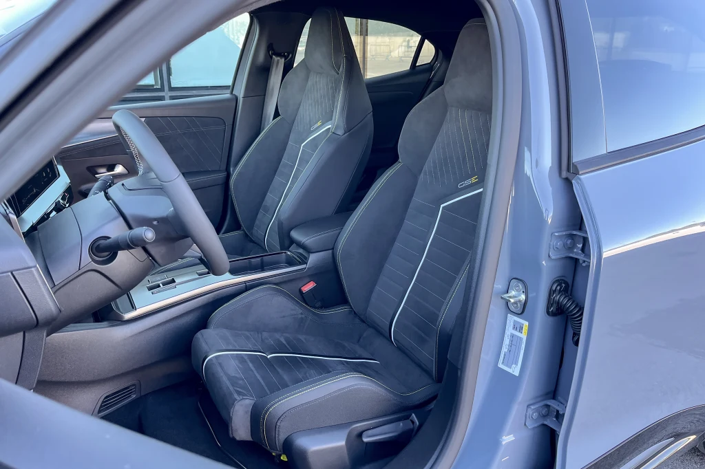 Nowoczesne wnętrze samochodu z czarnymi, sportowymi fotelami obszytymi kontrastową nicią oraz panelem sterowania i kierownicą pokrytą ciemnym materiałem.