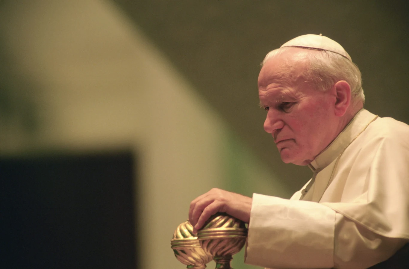 Jan Paweł II, 28.09.1994 r. Starszy mężczyzna w białej sutannie i piusce, z poważnym wyrazem twarzy, opiera dłonie na ozdobnym tronie.