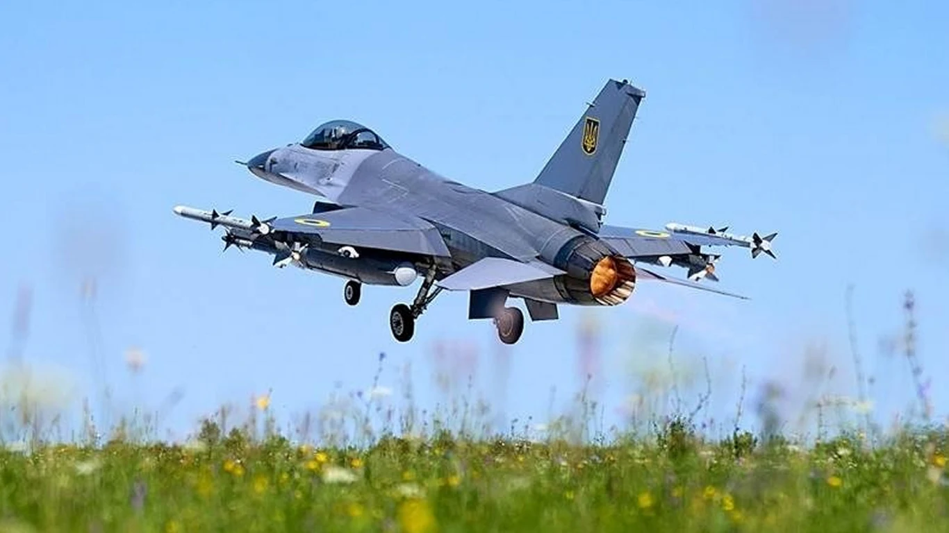 Ukraińcy pokazali, jak strącają z pomocą F-16 potężne rosyjskie pociski Ch-101 Myśliwiec wojskowy F-16 w locie tuż nad łąką, z widocznym pracującym silnikiem odrzutowym i uzbrojeniem pod skrzydłami na tle błękitnego nieba.